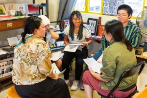 A small group gathers in a circle holding papers and smiling. 